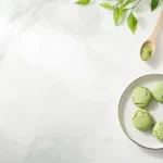 STYLE: Styled serving shot, overhead view | EMOTION: Warm and inviting | SCENE: A plate of baked matcha cookies served alongside a small cup of matcha latte, placed on a light wooden table. A linen napkin and a few scattered white chocolate chips complete the cozy scene | TAGS: High-end food photography, cozy, inviting, matcha, cookies, latte, green tea desserts | CAMERA: Nikon Z7 II | FOCAL LENGTH: Soft natural light highlighting textures and colors | PRODUCTION: Food stylist | TIME: Morning | LOCATION TYPE: Light wooden table with a rustic background | --ar 4:3