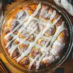 Freshly baked honey bun cake with a glossy glaze, surrounded by cinnamon sticks and powdered sugar on a wooden counter.