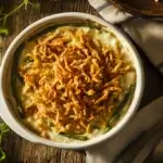 Freshly baked green bean casserole in a white baking dish, topped with crispy fried onions, served on a rustic table.