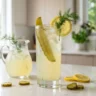 Pickle lemonade recipe in a tall glass with ice, dill pickle spear and lemon garnish
