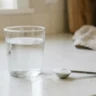 A glass of water with a measuring spoon of baking soda on a kitchen counter