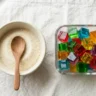 A bowl of unflavored gelatin powder next to colorful jello cubes
