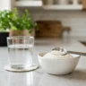 A glass of water next to a bowl of white fiber powder and a measuring spoon