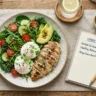 A balanced plate with grilled chicken, eggs, and leafy greens next to a notepad