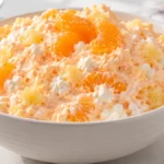 Mandarin orange jello salad with cottage cheese, whipped topping and pineapple in a white bowl