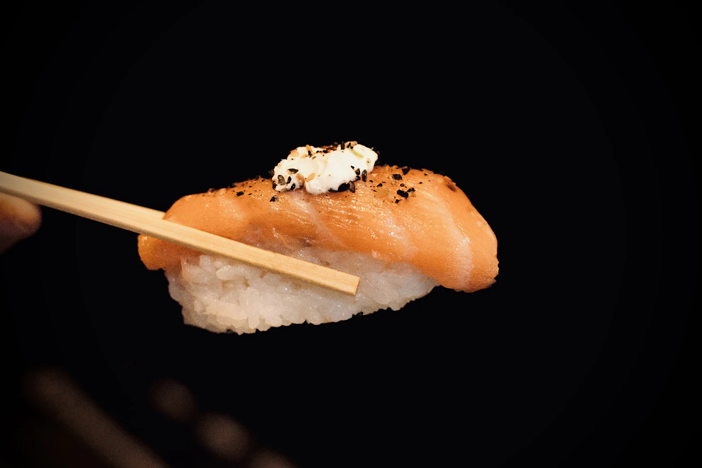 Salmon nigiri held with chopsticks showing fish and sushi rice