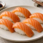 Salmon nigiri pieces with orange salmon slices over seasoned sushi rice on a ceramic plate
