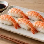 Cooked butterfly shrimp over sushi rice on a rectangular ceramic plate